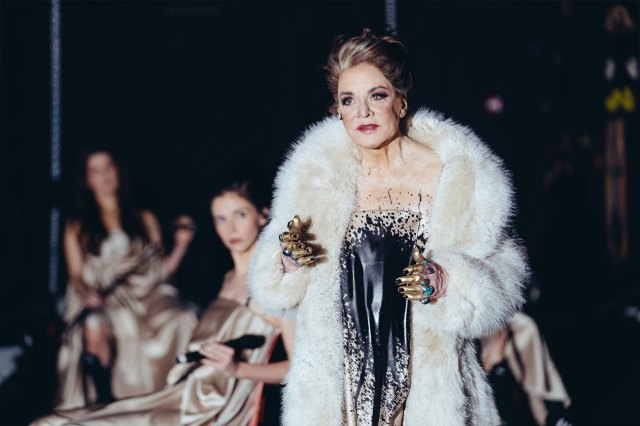 Une actrice sur scène dans un manteau de fourrure blanche et une robe blanche recouverte de peinture noire