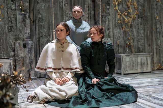 Three actresses kneel together in period costumes on stage
