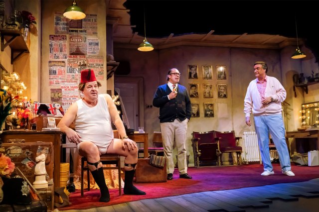 Trois acteurs sur scène sur un seigneur de vestiaires dans les coulisses, déguisé en comédiens Tommy Cooper Eric Morecambe et Bob Monkhouse