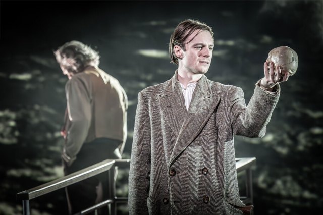 An actor in an overcoat, holding a skull on stage
