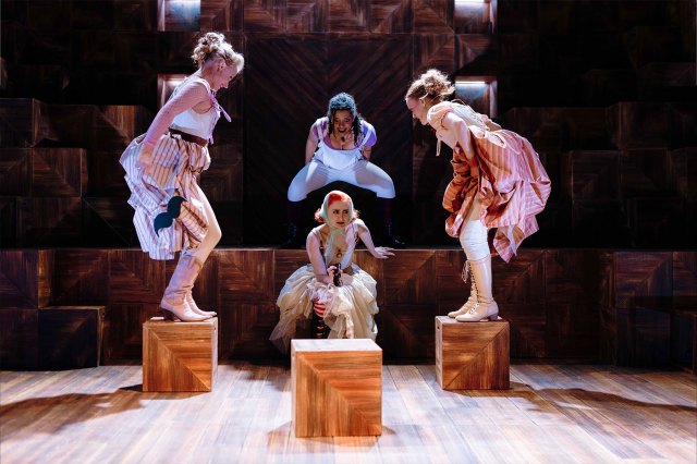 A group of actresses in period costumes on stage - two of them standing on top of wooden boxes