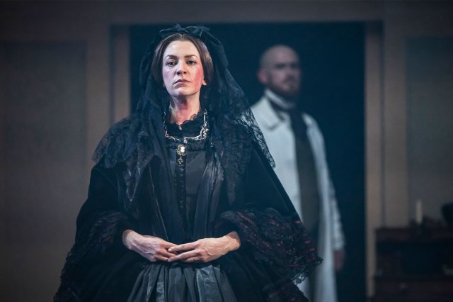 An actress on stage, dressed as Mary Todd Lincoln, and an actor in the background, wearing a white coat