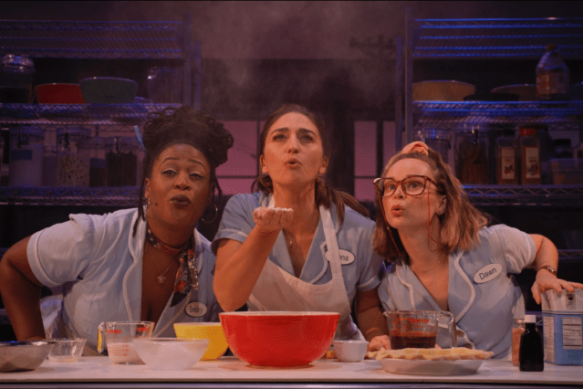 Three waitresses gather around a mixing bowl