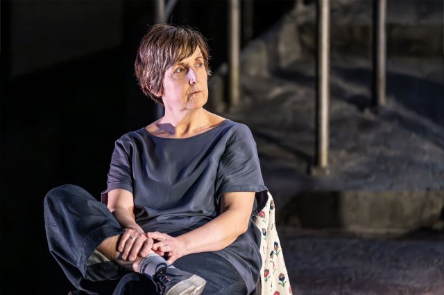 An actress sits down on stage with a concerned look on her face