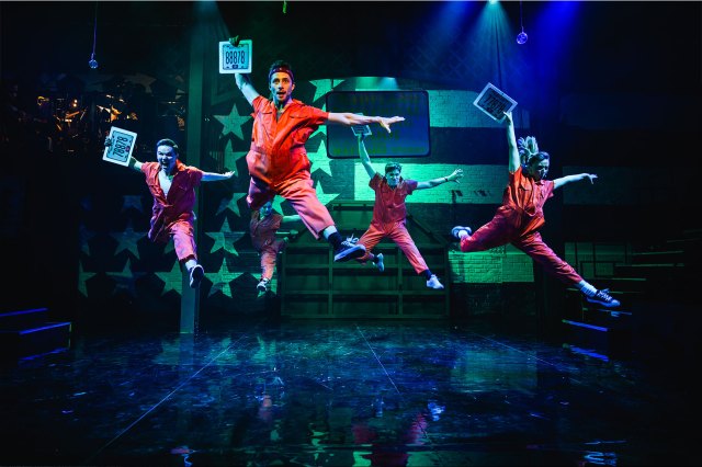 Cinq artistes dans les costumes d'Orange Prisoner, sautant dans les airs avec des plaques d'enregistrement de voiture entre les mains