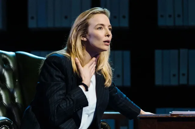 An actress on stage, wearing a black jacket and white blouse