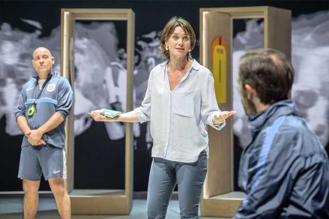 Une actrice se tient dans le vestiaire d'un footballeur, en conversation avec deux entraîneurs