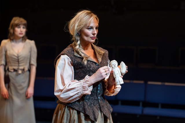 Une actrice sur scène dans la robe d'époque du XVIIe siècle, tenant une poupée blanche