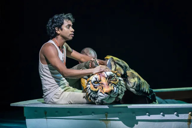 A young actor and a puppet tiger in a boat on stage