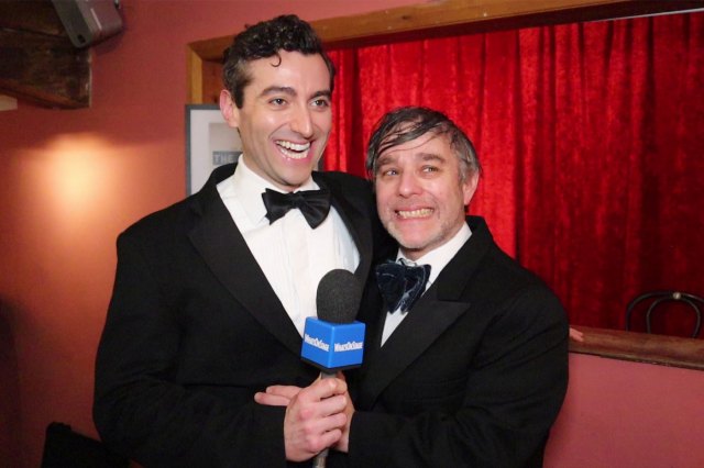 Two actors in black tie attire, holding a WhatsOnStage-branded microphone
