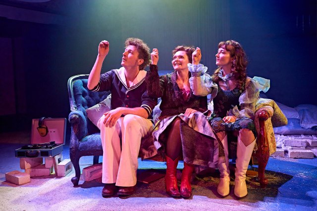 Three actors sitting on an ornate sofa with their right hands raised