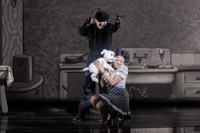 Une actrice, habillée en Betty Boop, embrasse une marionnette de chien blanc, exploité par un marionnettiste en vêtements noirs