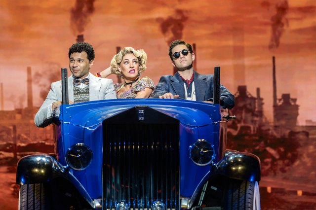 Deux acteurs et une actrice en tenue des années 1920 assis dans une voiture bleue des années 1920 sur scène
