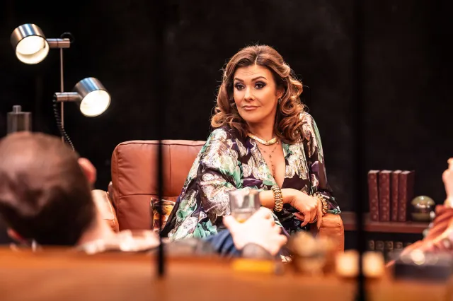 An actress sits on a brown leather seat on stage