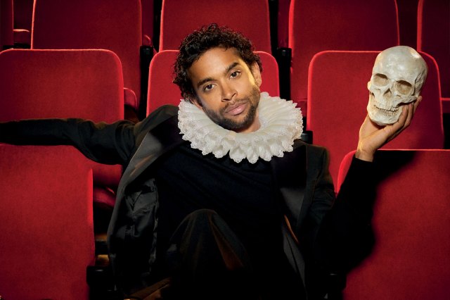 An actor in a Shakespearean costume, sat in an auditorium, holding a skull
