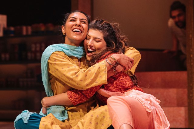 Two actresses in south Asian costumes embrace on stage