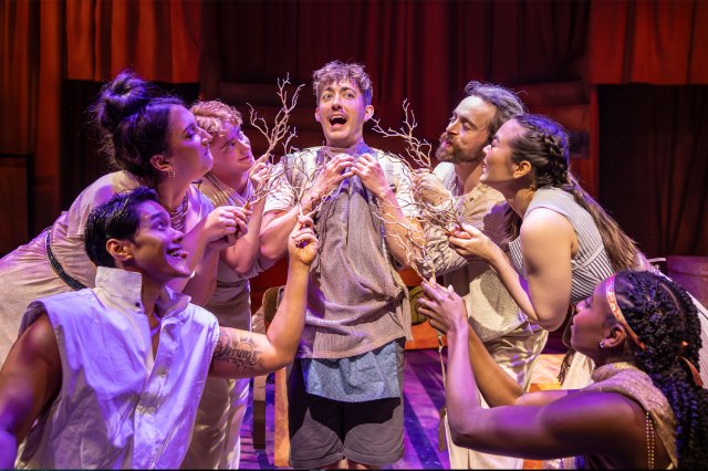 A group of actors gathered on stage, holding wooden twigs
