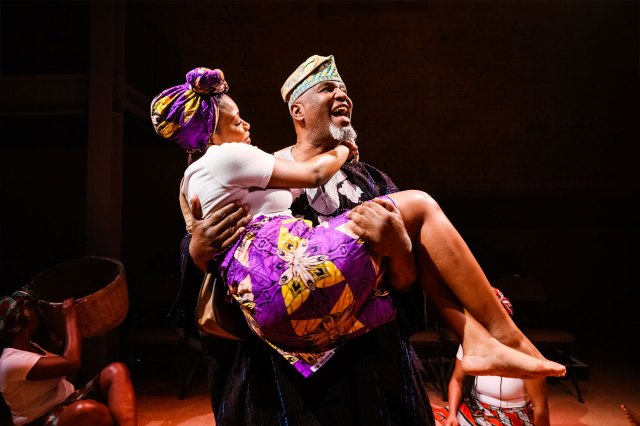 An actor carries an actress in his arms on stage, both in Nigerian attire.