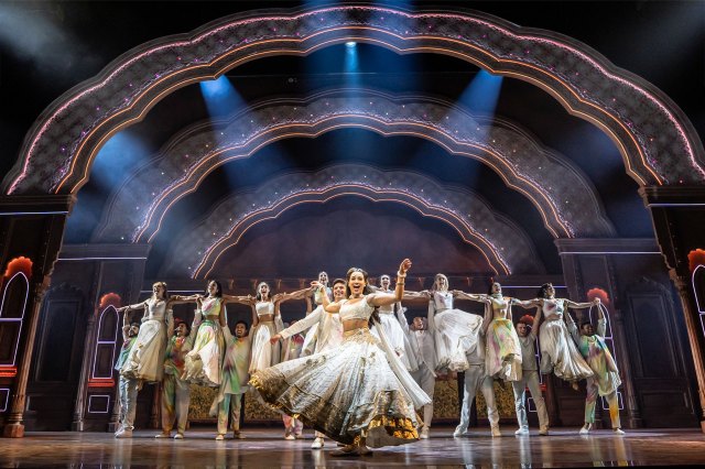 Une actrice principale et un groupe de danseurs de Bollywood sur scène en costumes blancs.