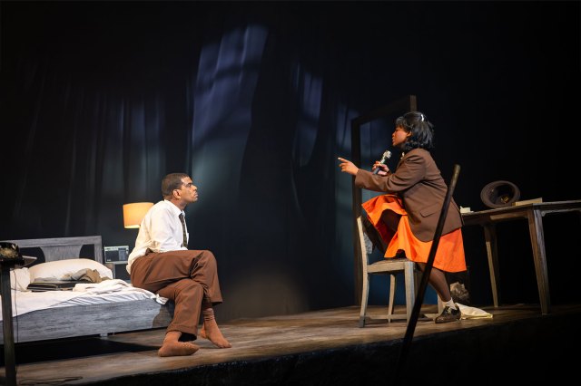 Un acteur dans une chemise blanche et un pantalon brun et une actrice en uniforme d'orange de femme de chambre dans une discussion sur une chambre d'hôtel se déroule sur scène