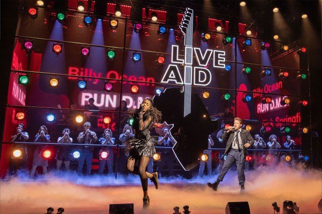 Two actors on stage dancing in front of a large Live Aid logo