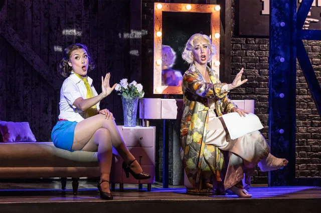 Two actresses on stage, sat together in a period Broadway dressing room