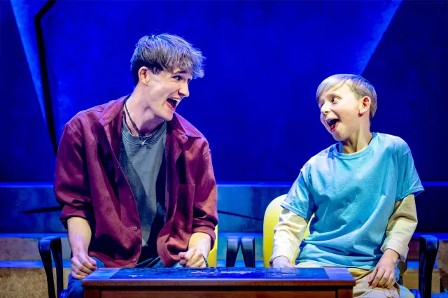 A young actor and a child actor laughing together on stage