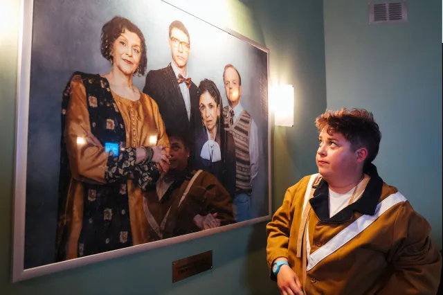 A young actor looks at a portrait of four people hanging on a wall