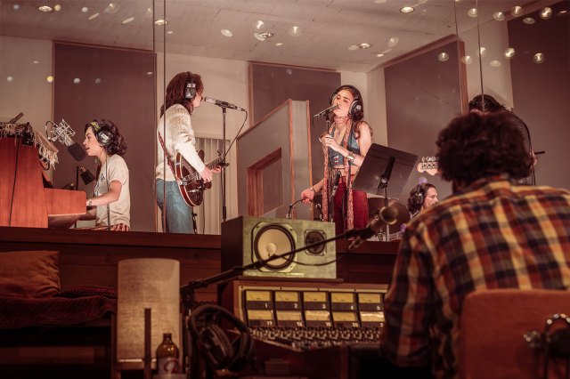 A scene from a play depicting a rock band and a sound engineer in a recording studio.