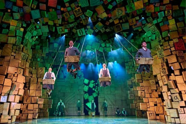Le casting de West End de Matilda Swing sur des balançoires en bois contre les blocs de lettres en bois