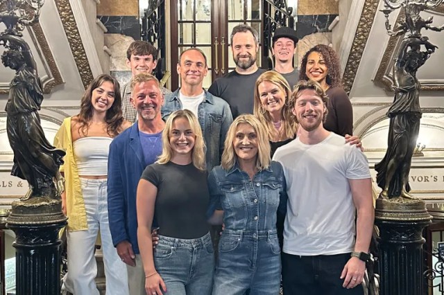 Une photo de groupe du nouveau casting de mamma mia alors qu'ils se tiennent et sourient dans des escaliers